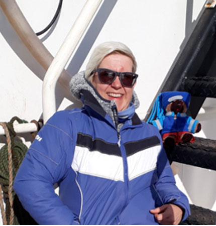 A smiling Elaine Mitchell relaxing aboard a research vessel donning Arctic clothing