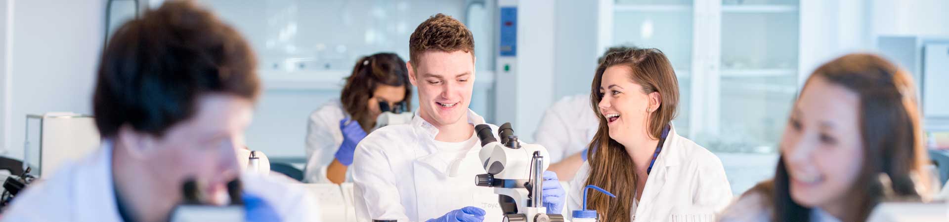This picture shows a row on marine science students in lab coats in a teaching laboratory having fun with microscopes