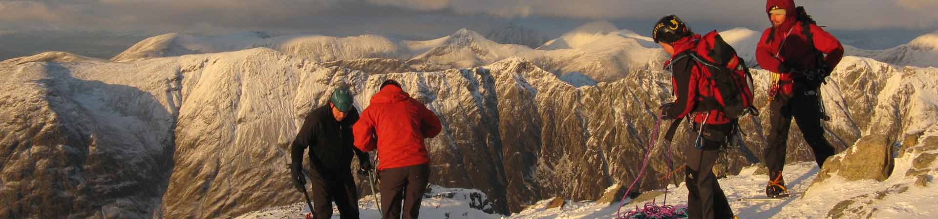 Four students mountaineering in the Scottish Highlands during winter with snow covered mountains behind them.