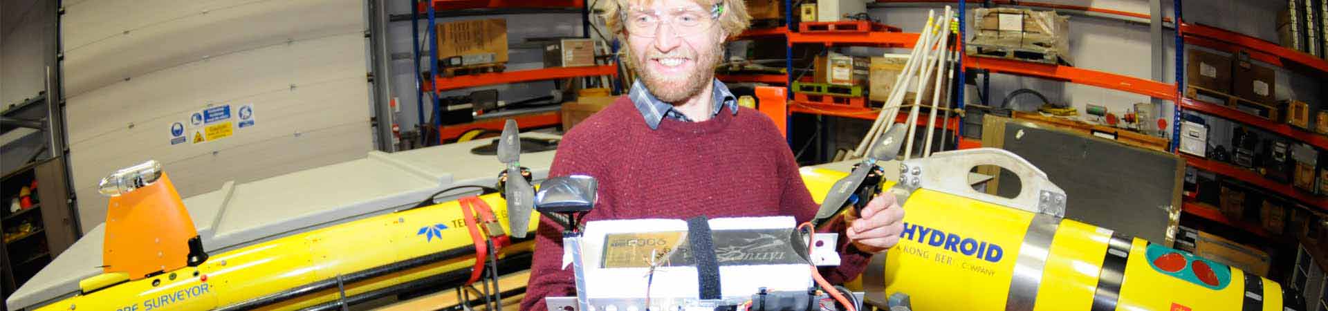 Technician with research UAV surrounded by underwater robots