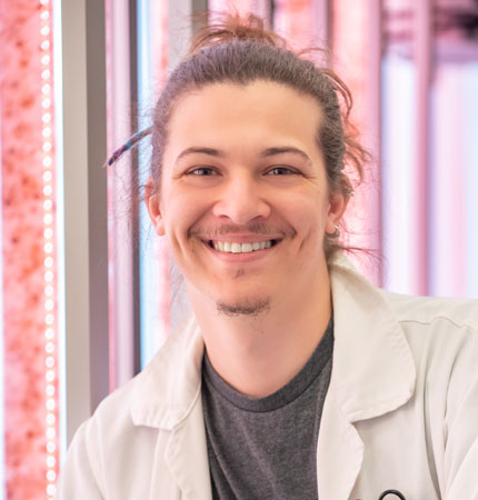 Picture of PhD student Alberto Rock wearing a lab boat in front of red algal cultures in tubes