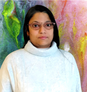 
        Puja Kumari wearing a white jumper in front of a colourful background
        