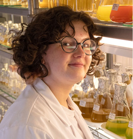 Young scientist with curly dark hair inside an algal culture collection walk-in fridge