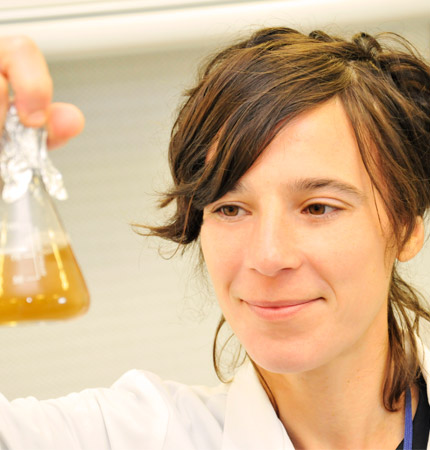 
        A smiling Ceci looking at a flask with diatoms
        