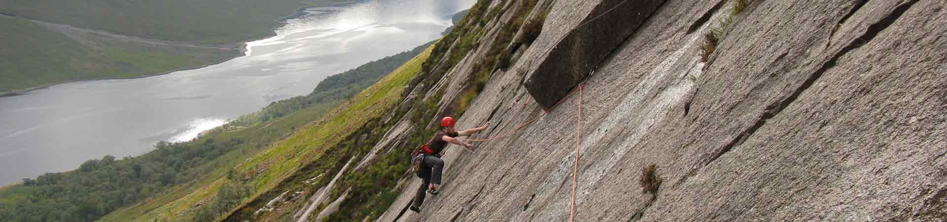 Student climbing up a wall in the Scottish Highlands, roped up with helmet