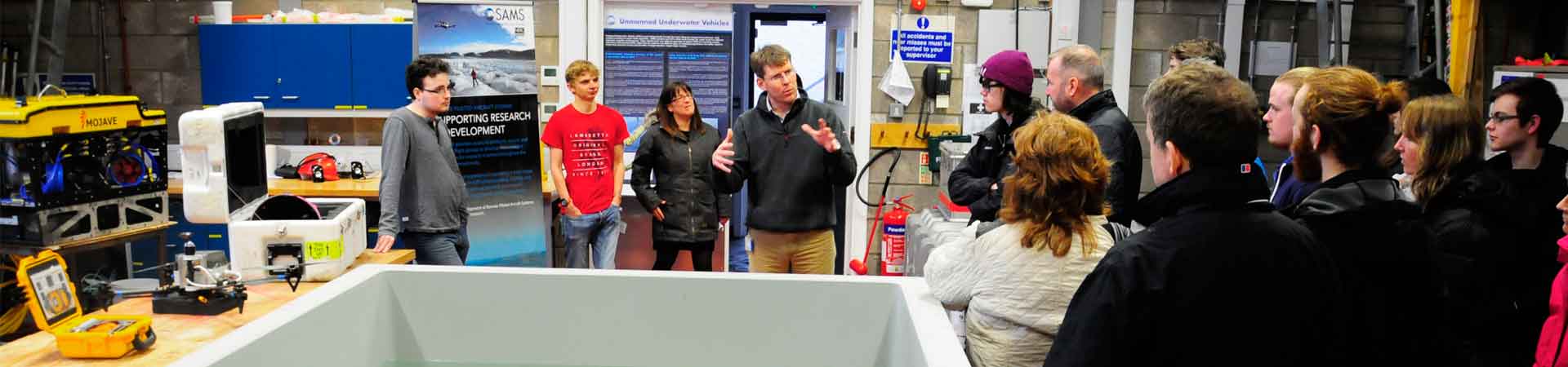 Picture of applicants with their families in our robotics facility with a lecturer and two students