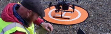 Man in high vis using laptop on beach with drone behind