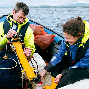 two researchers on a boat, taking samples at the SAMS seaweed farm
